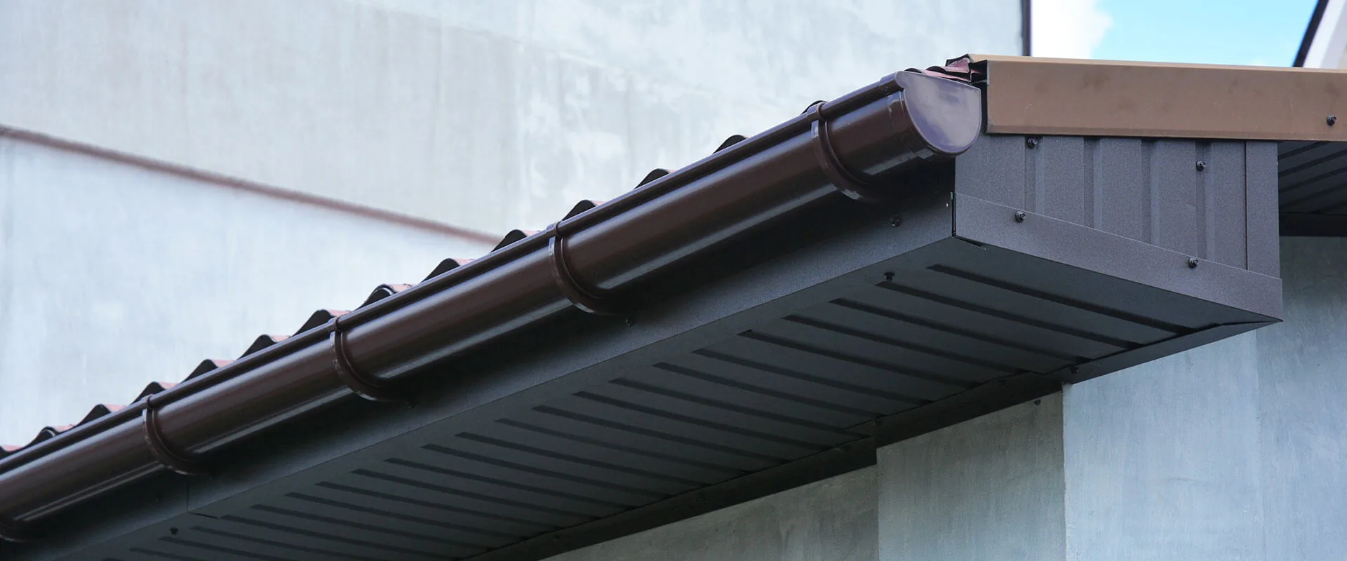 Brown metal gutter system installed along roof edge of residential building.